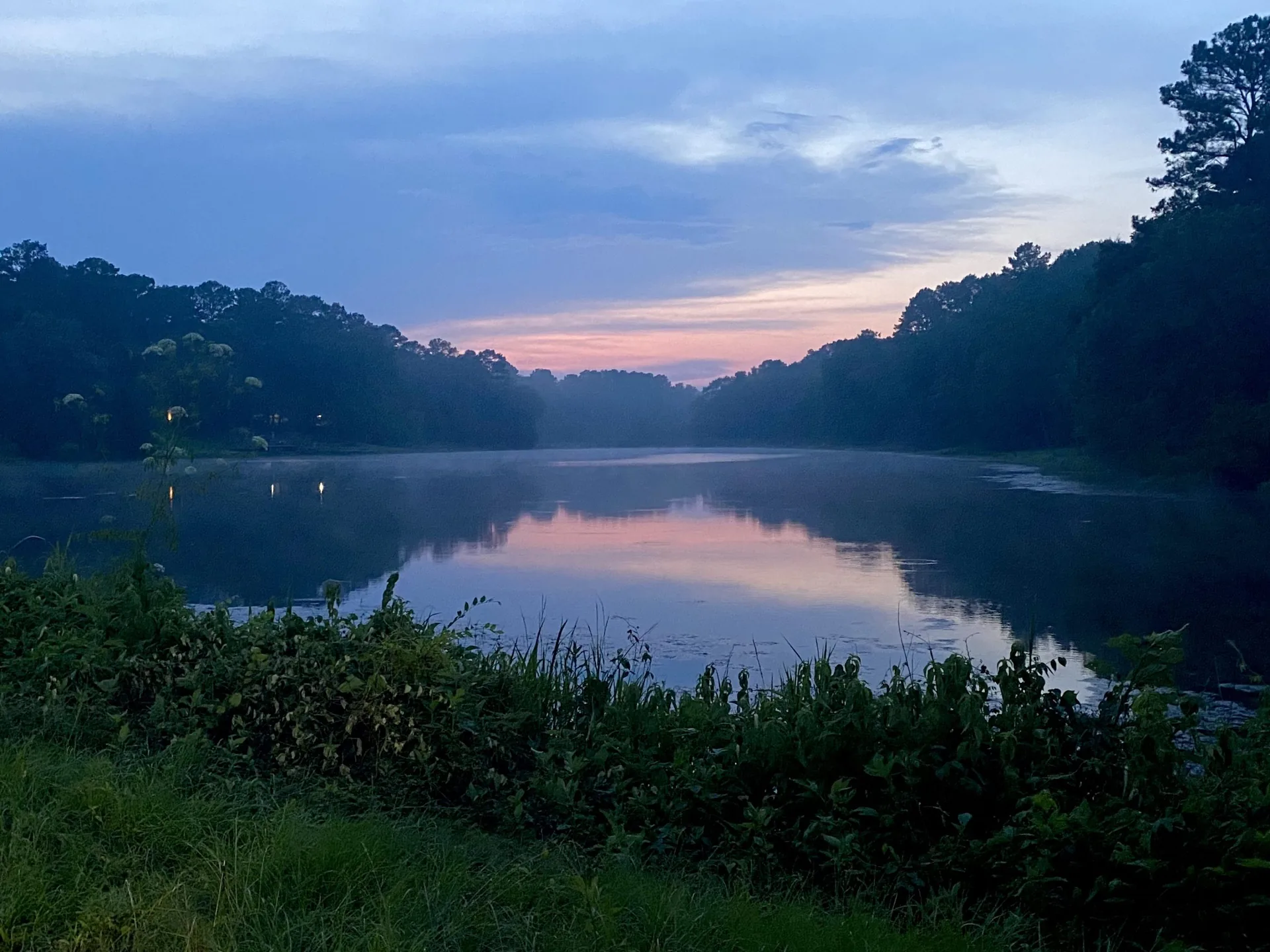 A private Eastdale Acres lake at dawn, a soft pink and blue sky reflected in the still water framed by trees and tall grass